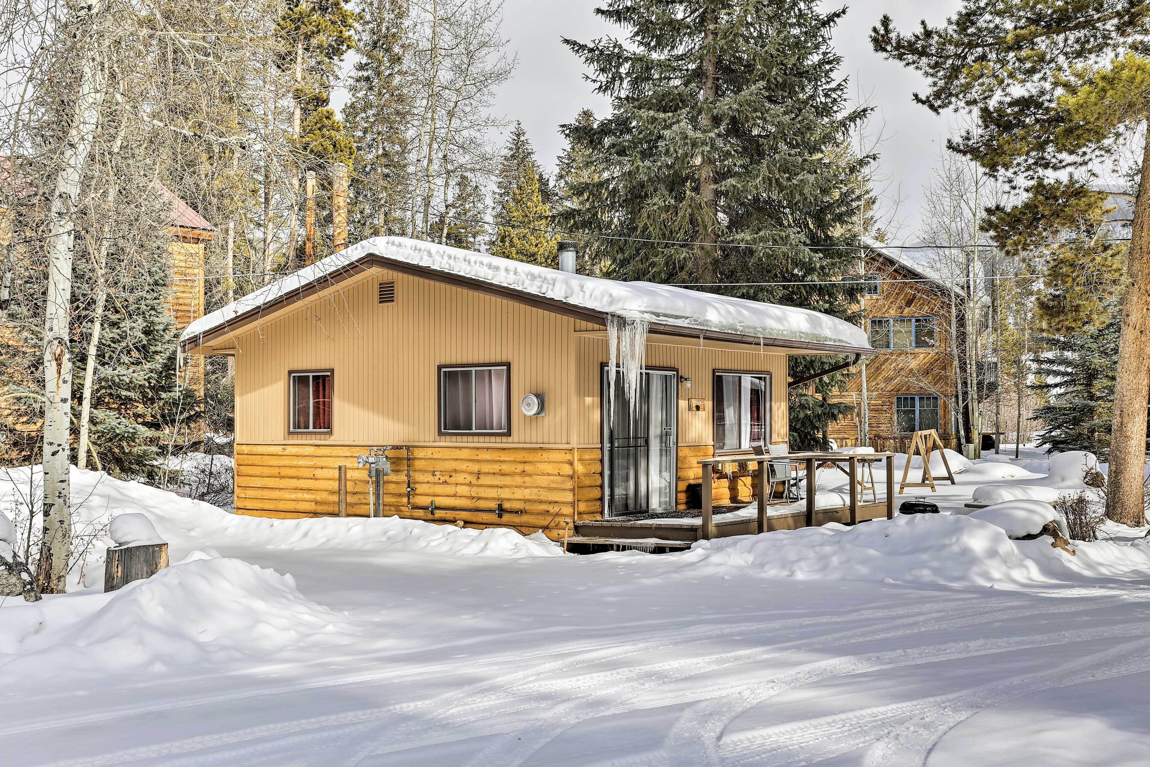 Una cabaña de madera con un porche cubierto y un patio cubierto de nieve.