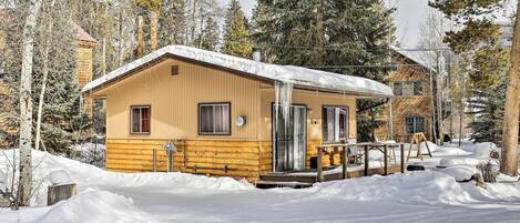 Una cabaña de madera con un porche cubierto y un patio cubierto de nieve.