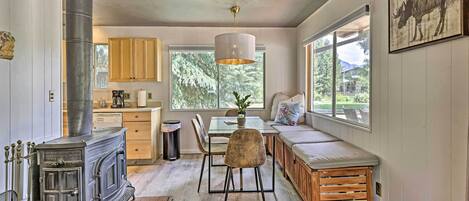 A cozy interior with a wood-burning stove, a dining area, and a large window offering a view of the outdoors.