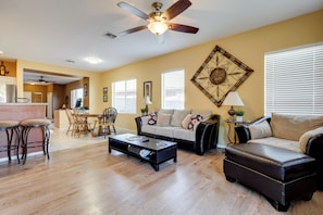 A living room with a sofa, coffee table, and chairs. There is a dining area with a table and chairs. A ceiling fan and a decorative wall piece are visible. - Superstition Mtn Views! Gold Canyon Gem w/ Hot Tub (Gold Canyon)