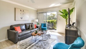 Ein modernes Wohnzimmer mit einem schwarzen Ledersofa, einem blauen Sessel, einem Holztisch und einer großen Pflanze.
