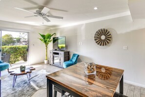 A modern living room with a dining table, blue chairs, a ceiling fan, a TV, and a large potted plant.