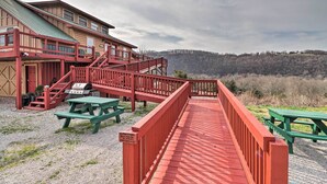 Una terraza de madera con mesas de picnic, una escalera roja y un edificio con techo de metal.