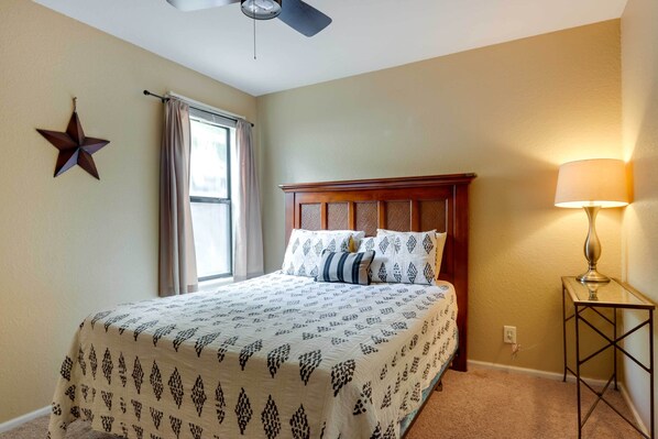 A bedroom with a bed, a star decoration, a window with curtains, a bedside lamp, and a ceiling fan.