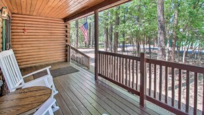 A wooden deck with a table and chairs, overlooking a forested area with trees and a flag. - Pinetop-lakeside Cabin w/ Deck: Hike, Ski & Golf (Pinetop)