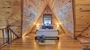 Een gezellig slaapkamer op zolder, met een schuine kap, een bed met kussens en dekens, twee nachtlampjes en een raam met zonwering.
