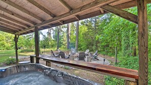 Een hottub onder een houten pergola met uitzicht op een bebost gebied en buiten zitplaatsen.