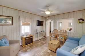 A room with a wooden paneled wall, a ceiling fan, a television, a sofa, a chair, a small table, and a wicker basket. - Deck & Indian River Bay Views: Coastal Cottage (Millsboro)