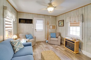 A cozy living room with a blue sofa, beige armchairs, a wooden coffee table, and a built-in fireplace. - Deck & Indian River Bay Views: Coastal Cottage (Millsboro)