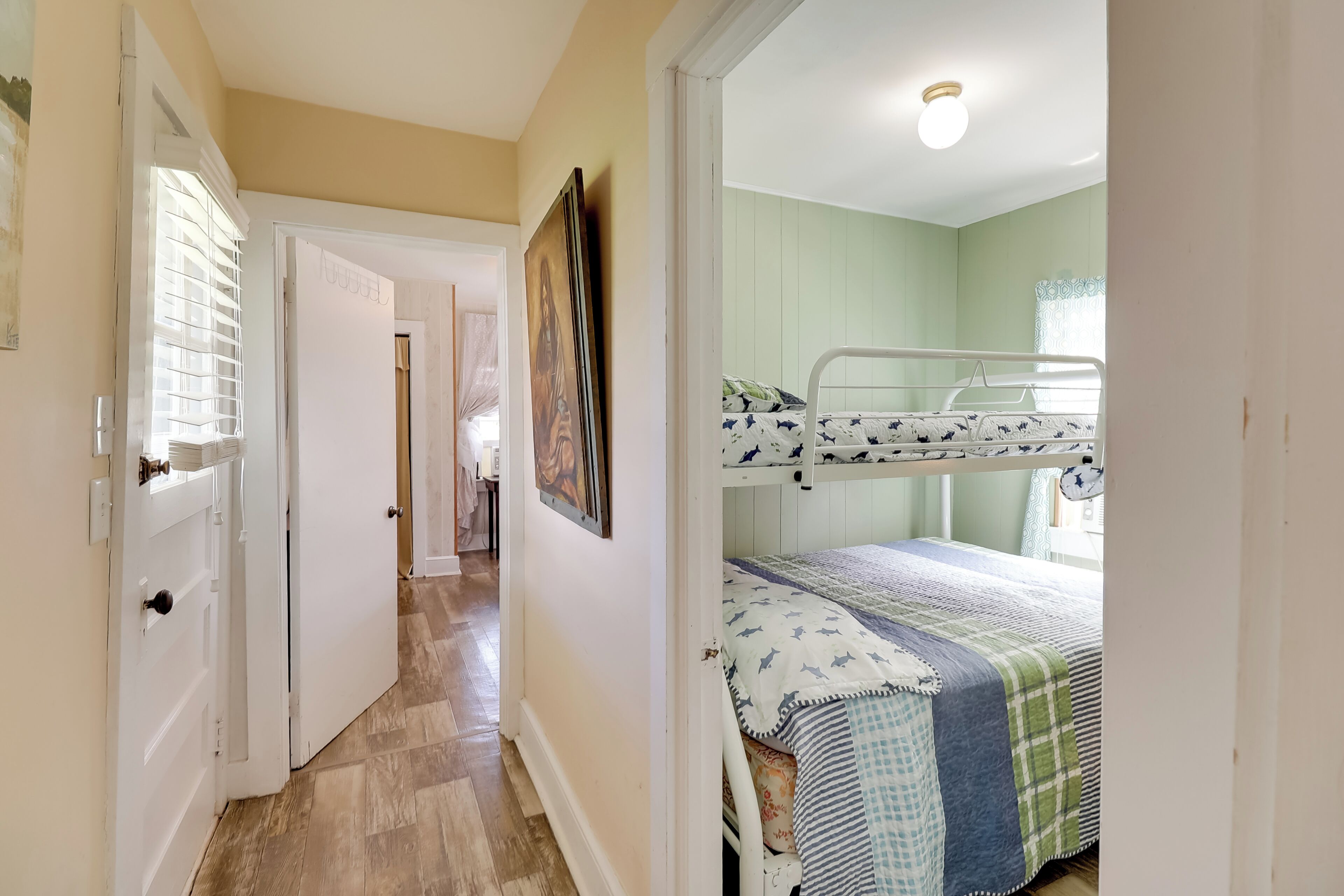 A bedroom with bunk beds, a door leading to another room, and a hallway with a light fixture.