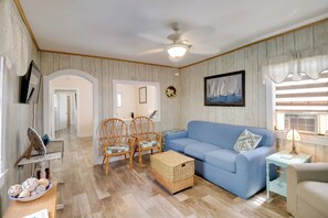 A living room with a blue sofa, wicker baskets, wicker chairs, a ceiling fan, and a framed picture on the wall. - Deck & Indian River Bay Views: Coastal Cottage (Millsboro)
