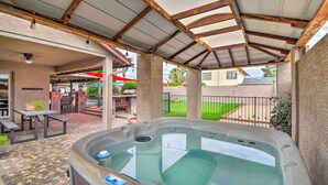 En overdækket patio med jacuzzi, picnicborde og udsigt over et boligområde.