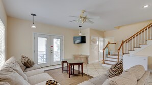 A living room with a sofa, a dining table, and a staircase. - Orange Beach Family Duplex w/ Deck < 1 Mi to Shore (Orange Beach)