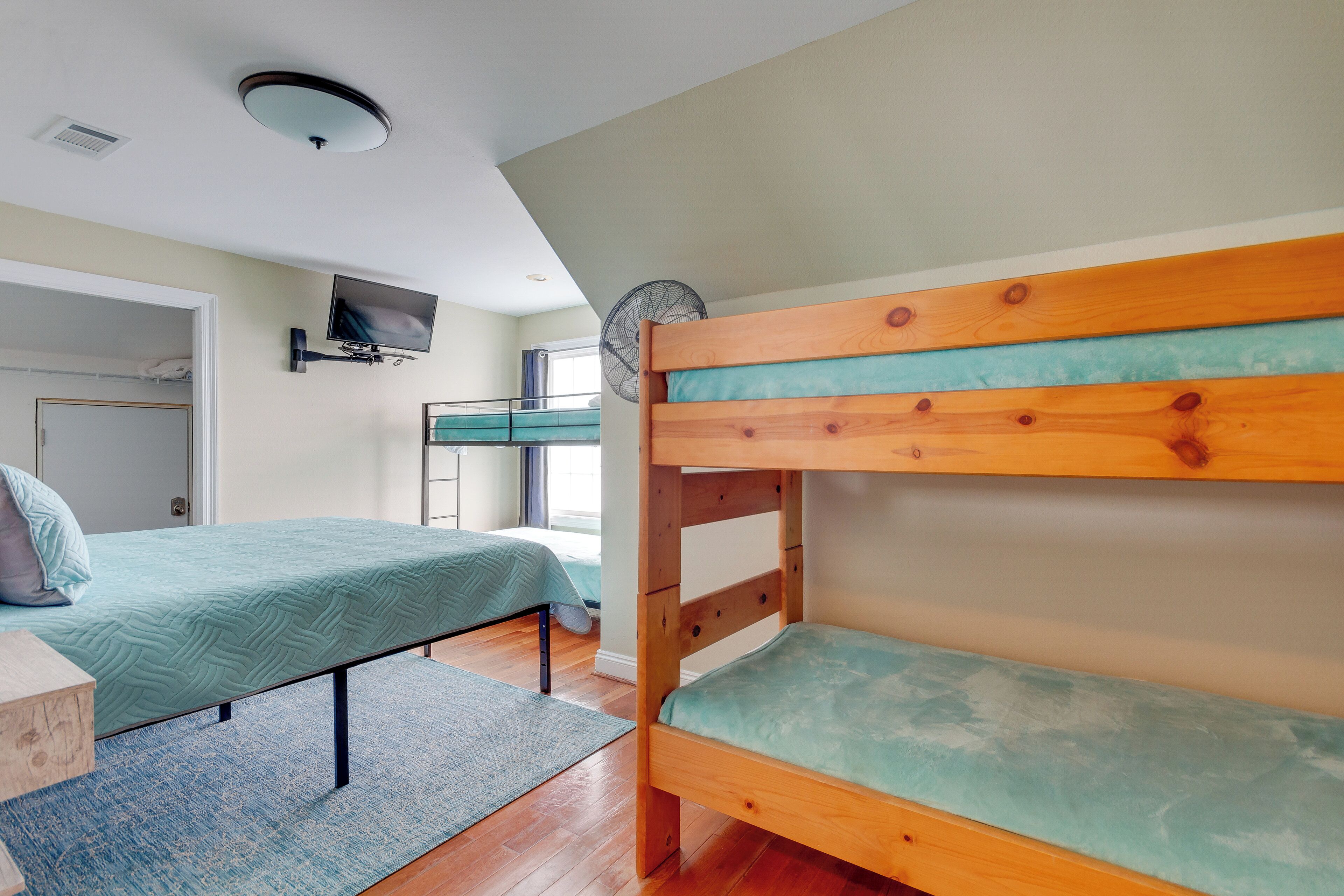A room with bunk beds, a television mounted on the wall, and a ceiling fan.