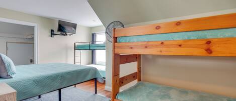 A room with bunk beds, a television mounted on the wall, and a ceiling fan.