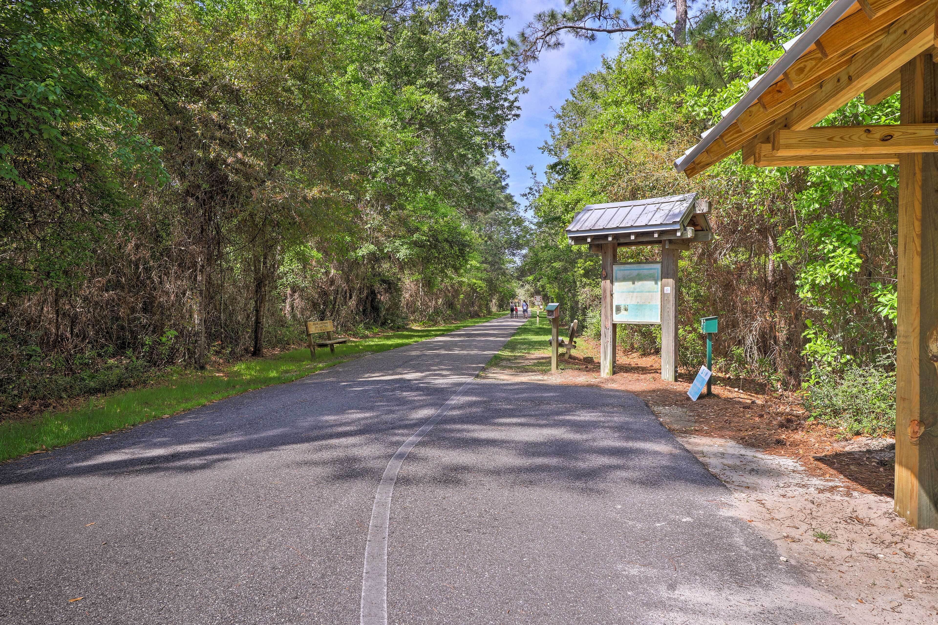A paved pathway leading to a wooden structure with a signboard, surrounded by dense trees.