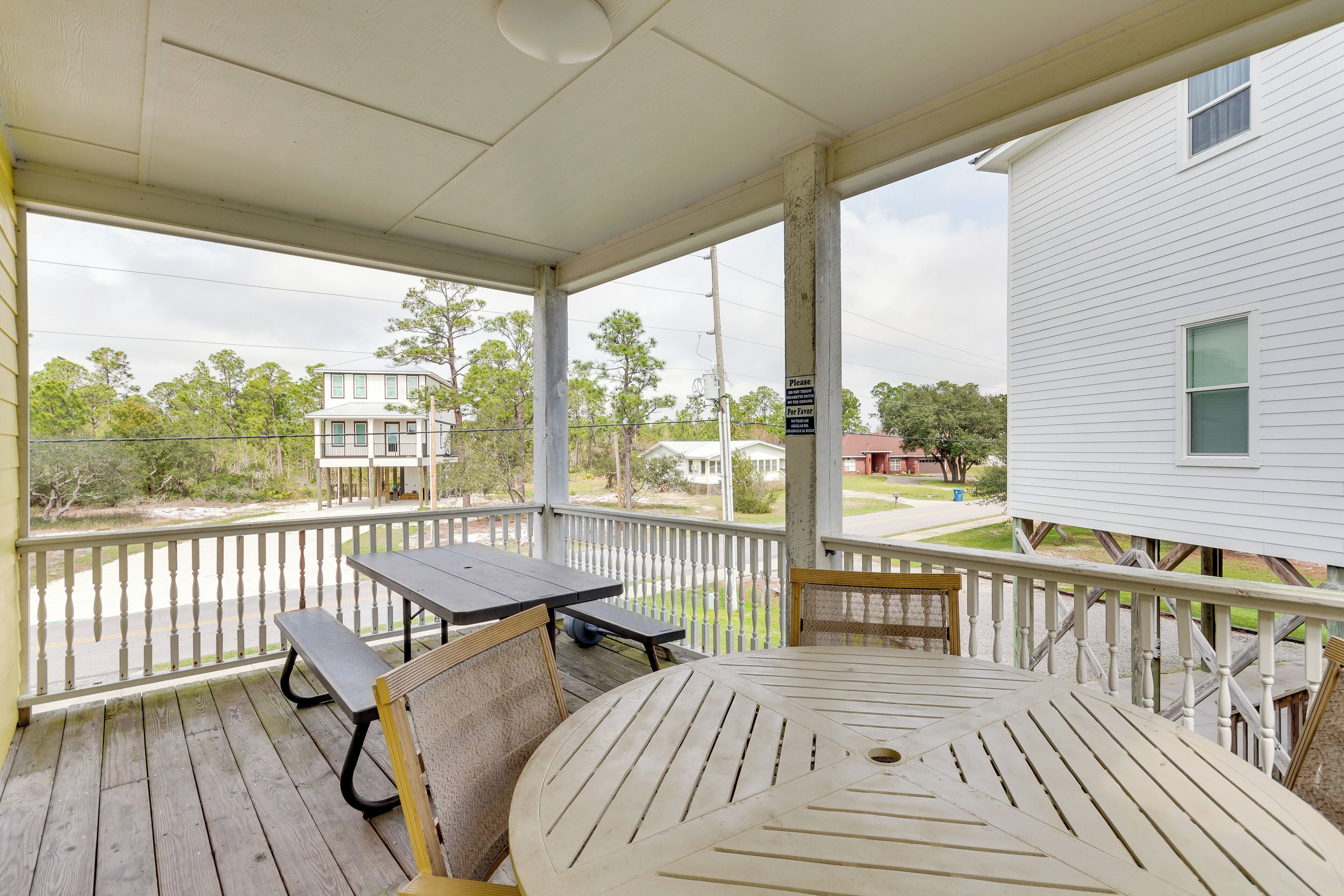 A covered porch with a table and benches, overlooking a residential street.