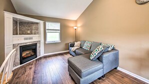 A living room with a fireplace, a grey sofa, and a clock on the wall. - Family-friendly Coatesville House w/ Fire Pit (Coatesville)