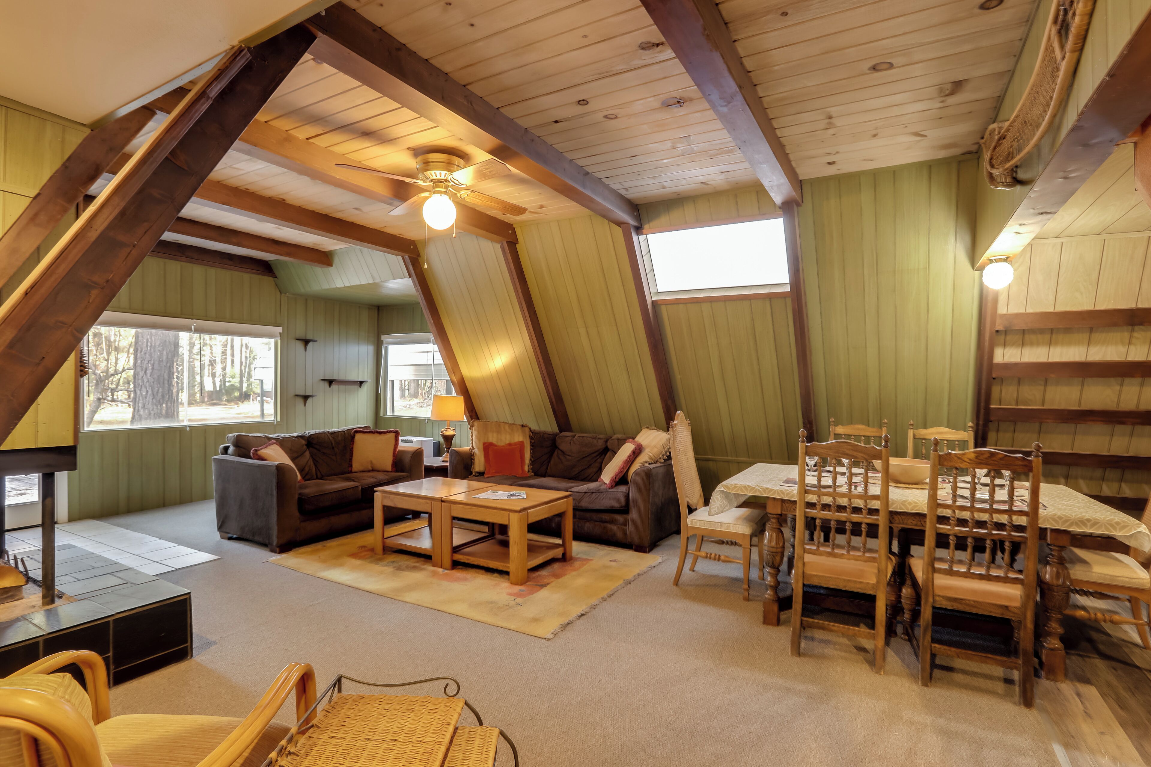 A cozy attic-style living room with a wooden ceiling, a fireplace, and a dining area with wooden chairs and a table.