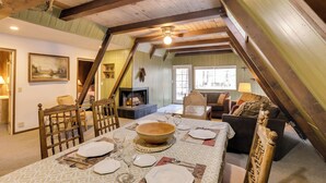 Un comedor con una gran mesa de madera dispuesta para una comida, una chimenea y un rincón de estar acogedor con sofá y sillones.