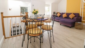 Amplia sala de estar con una mesa de comedor de madera, cuatro sillas, un sofá morado y una pared de acento amarilla.