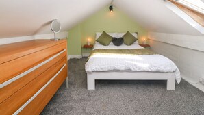 Un dormitorio con techo inclinado, un aparador de madera, una cama con ropa de cama blanca, dos mesitas de noche con velas y un tragaluz.
