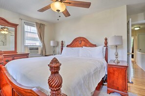A bedroom with a large bed, wooden headboard, two bedside tables with lamps, a ceiling fan, a window with curtains, and a mirror. - Suburban Home w/ Backyard Patio < 7 Mi to Dtwn! (Lansdowne)