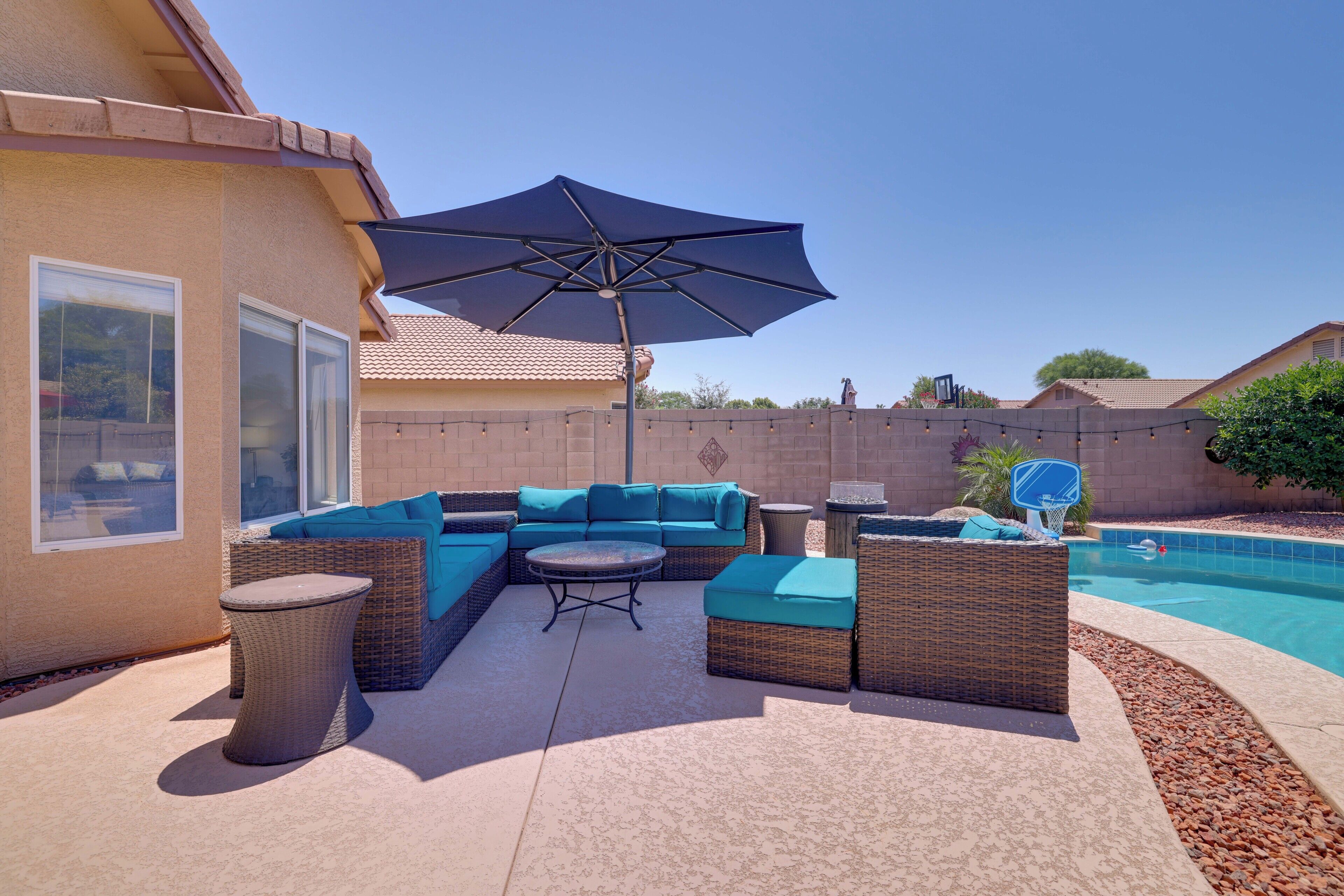 A backyard with a pool, outdoor furniture, and a large umbrella.