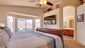 Un dormitorio con una cama grande, ventilador de techo, televisión y vistas al exterior.