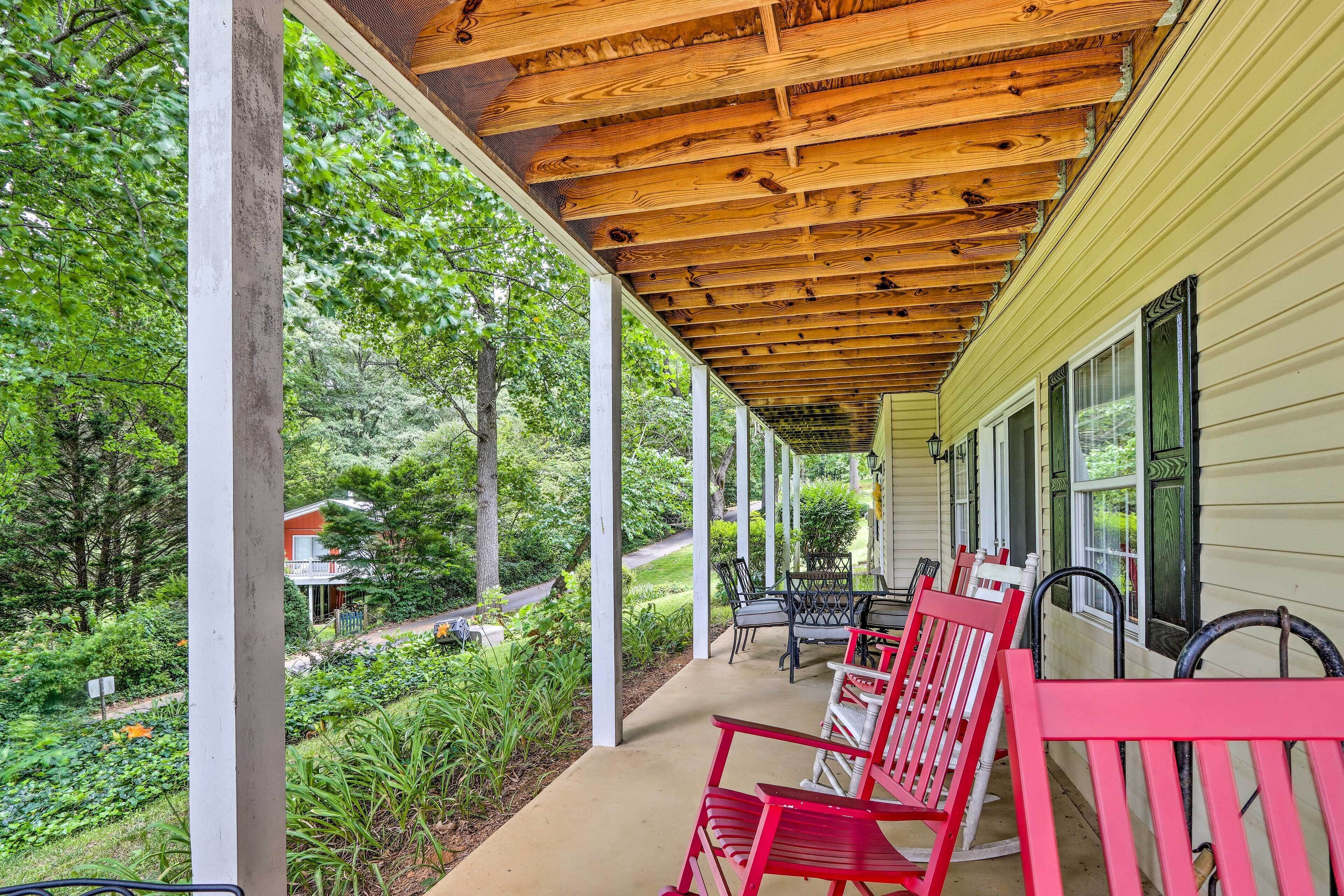 A covered porch with wooden beams, red chairs, and a view of a lush garden and a house in the background.