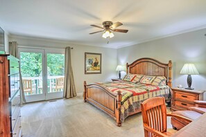 A bedroom with a wooden bed, a ceiling fan, a nightstand, a chair, and a view of the outdoors through a sliding glass door. - Lake Chatuge Retreat w/ Dock & Mtn Views! (Hayesville)