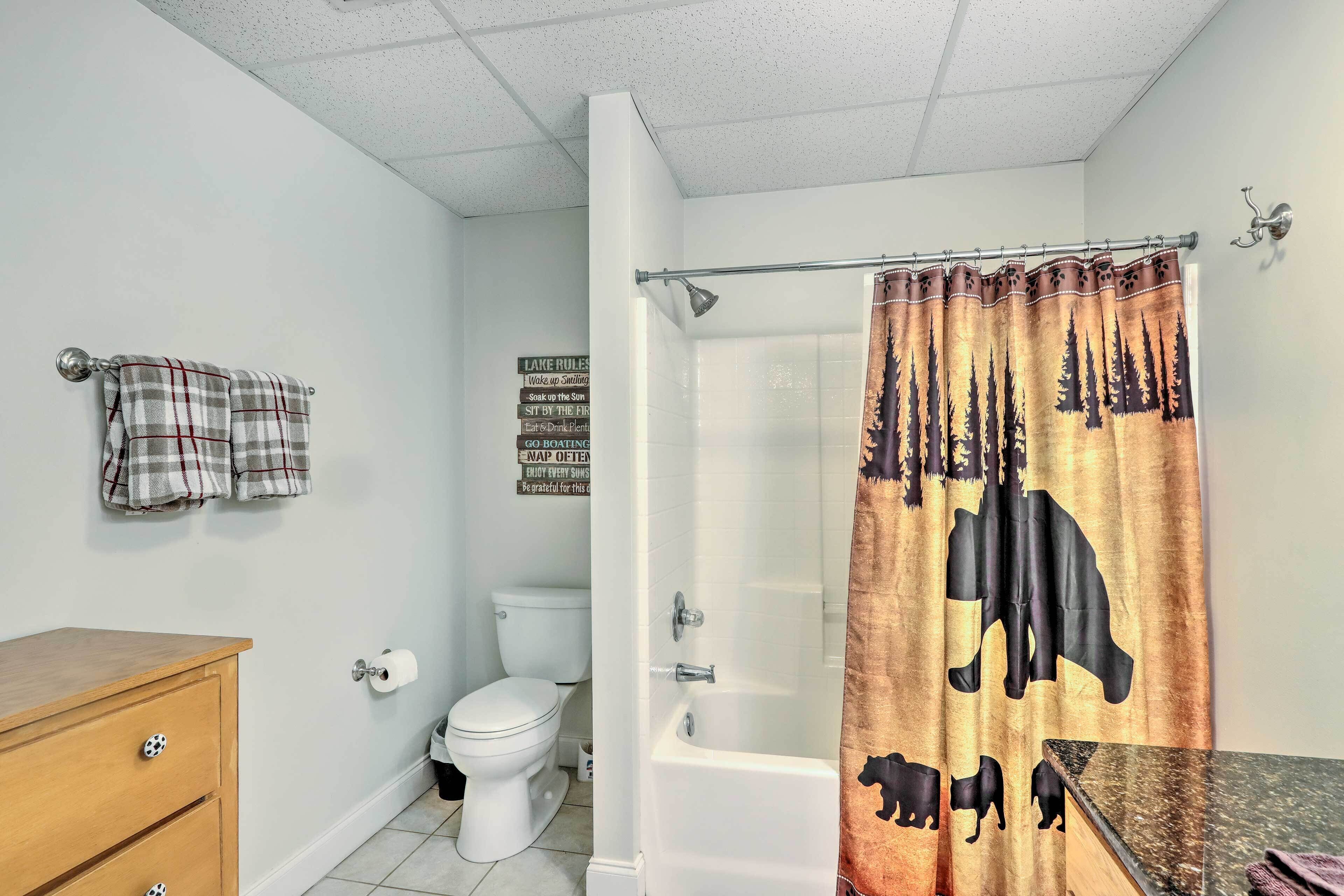 A bathroom with a toilet, a bathtub, a wooden cabinet, and a shower curtain with animal prints.