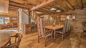 A rustic log cabin interior with a wooden dining table, chairs, and a staircase leading to another level. - 5 Mi to Hiking: Custom Cabin w/ Deck in Arnold! (Arnold)