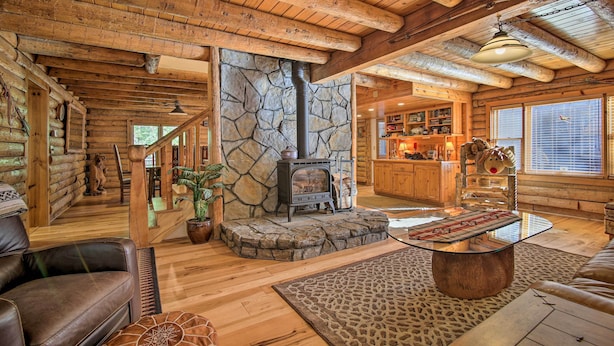 A log cabin interior with a stone fireplace, wooden furniture, and a kitchen area. - 5 Mi to Hiking: Custom Cabin w/ Deck in Arnold! (Arnold)