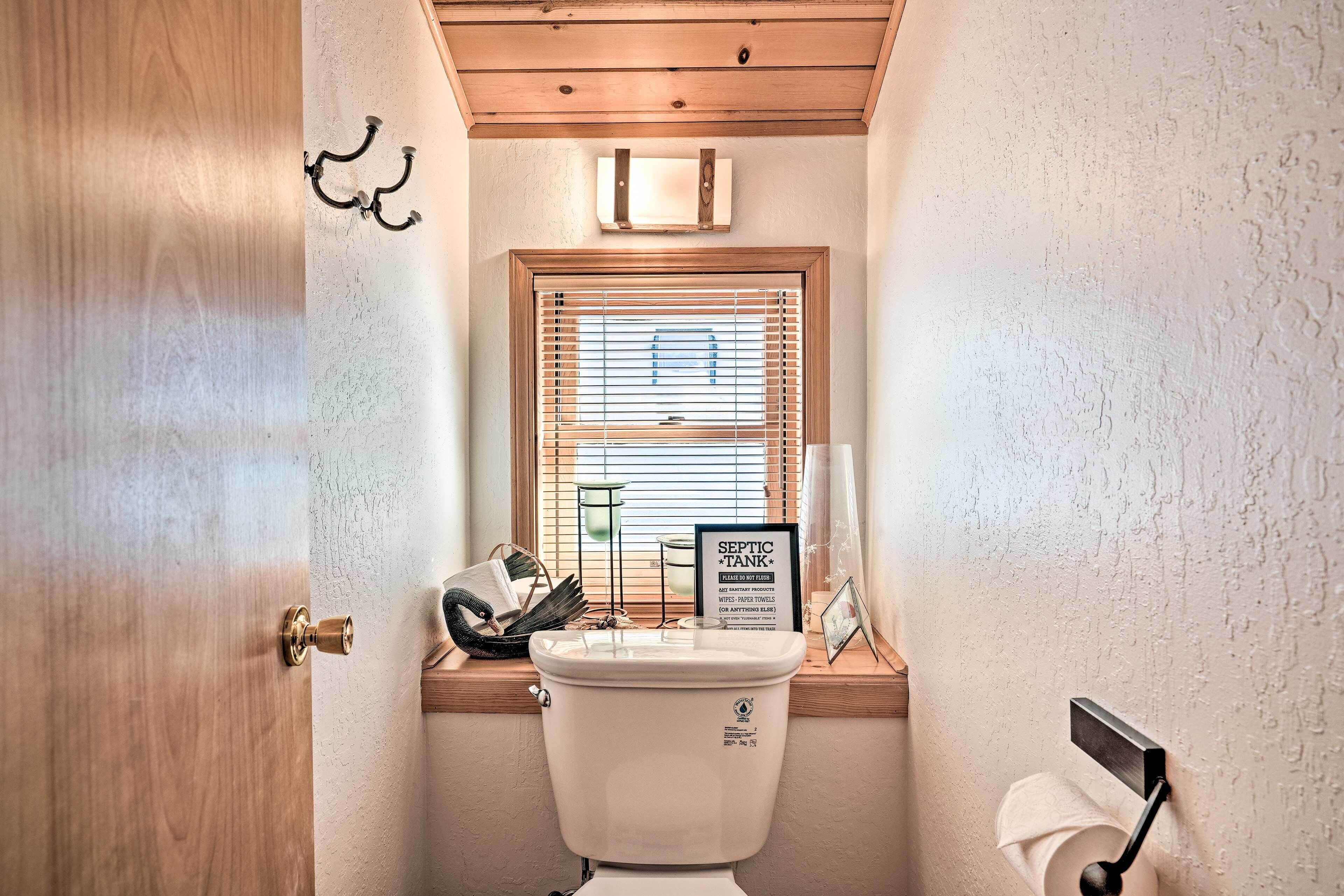 Une petite salle de bain comprenant des toilettes, une fenêtre avec des stores, un porte-serviettes et un panneau indiquant la présence d'une fosse septique.
