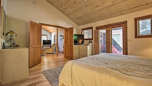 A bedroom with a large bed, wooden ceiling, and a TV. There are wooden doors and a desk with a lamp. - 5 Mi to Hiking: Custom Cabin w/ Deck in Arnold! (Arnold)