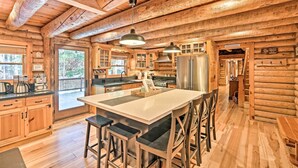 A log cabin kitchen with a large island, bar stools, wooden cabinets, and a stainless steel refrigerator. - 5 Mi to Hiking: Custom Cabin w/ Deck in Arnold! (Arnold)