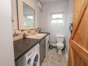 Un baño pequeño con lavamanos, espejo, inodoro y lavadora.