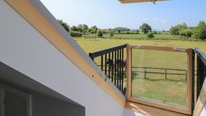 Un balcon avec une porte vitrée donnant sur un champ verdoyant où paissent des chevaux.