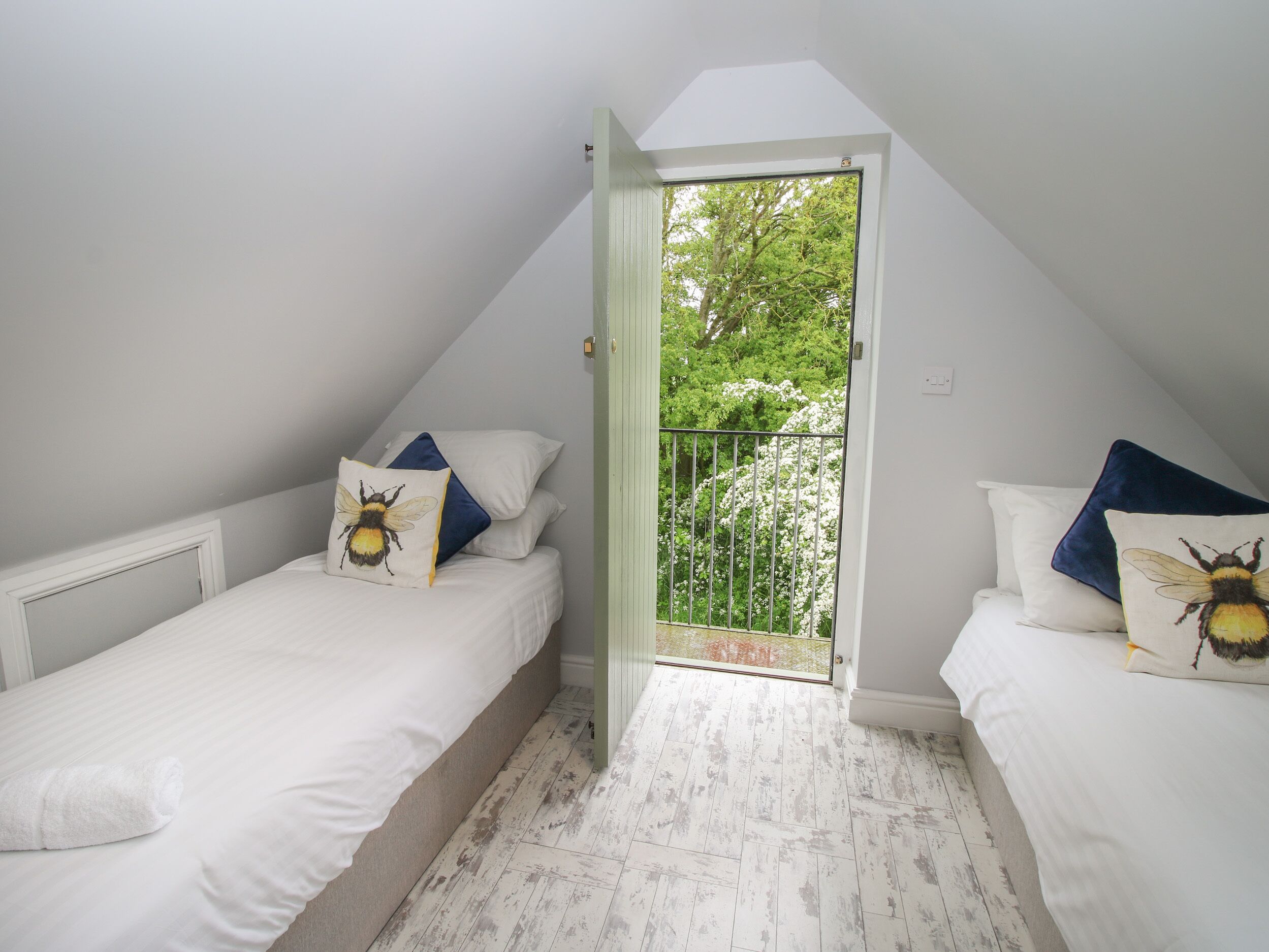 A small, white, attic-style bedroom with two single beds, each with a bee-themed pillow.