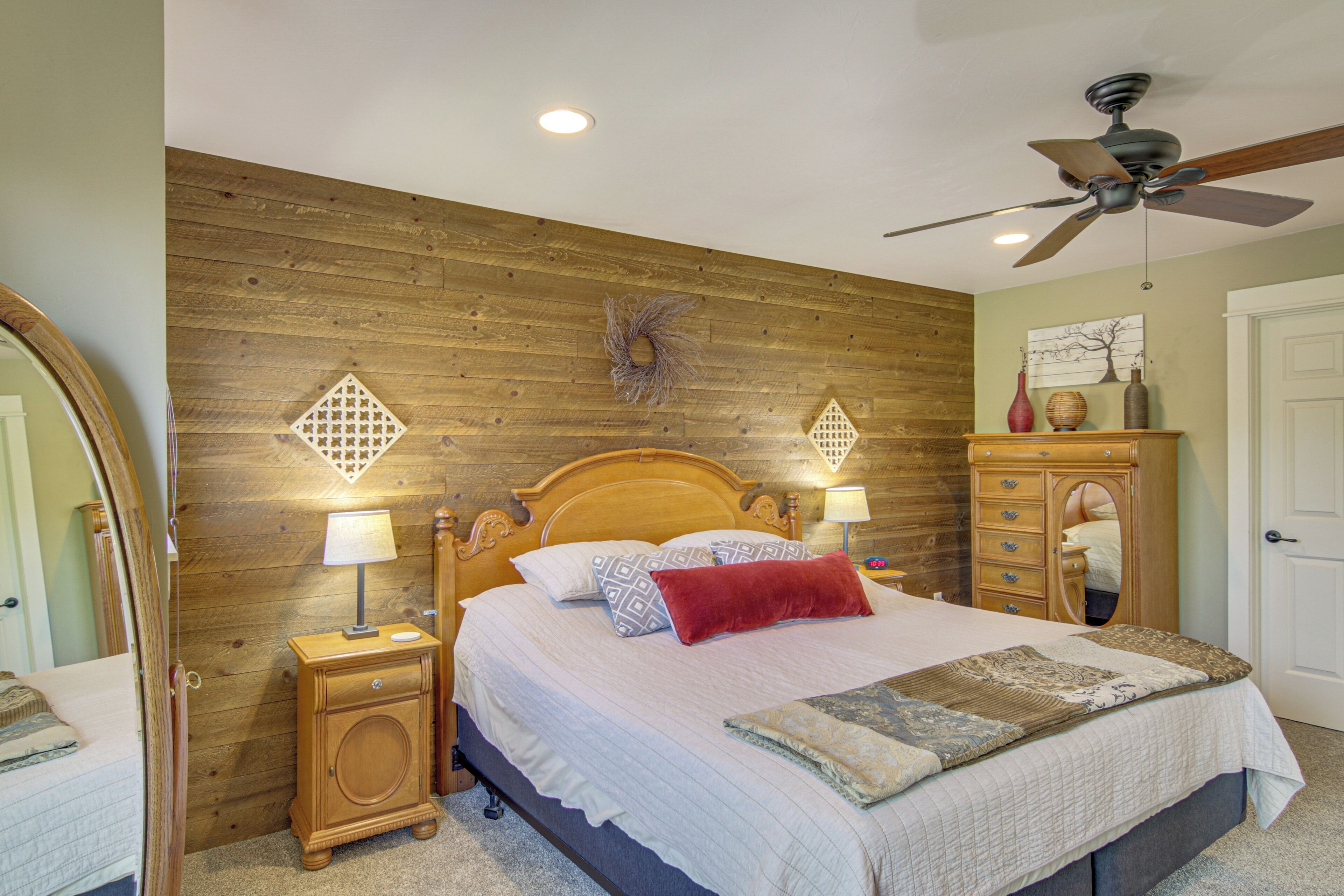 Quarto com cabeceira de madeira, cama com roupa de cama branca, duas luminárias de cabeceira, mesa de cabeceira, cômoda e ventilador de teto.