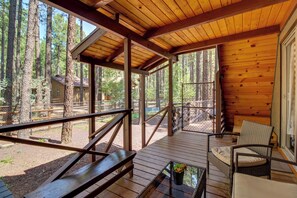 A wooden deck with a glass table and chairs, overlooking a forested area.
