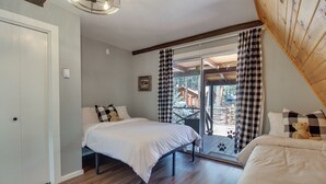 A bedroom with two beds, a window with checkered curtains, and a view of a wooden deck and trees. - The Silly Goose A-frame Cabin in Pinetop-lakeside (Pinetop)