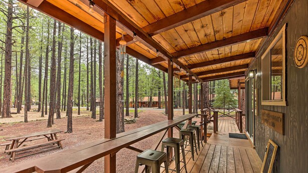 An outdoor wooden deck with picnic tables and bar stools, surrounded by a forest. - The Silly Goose A-frame Cabin in Pinetop-lakeside (Pinetop)