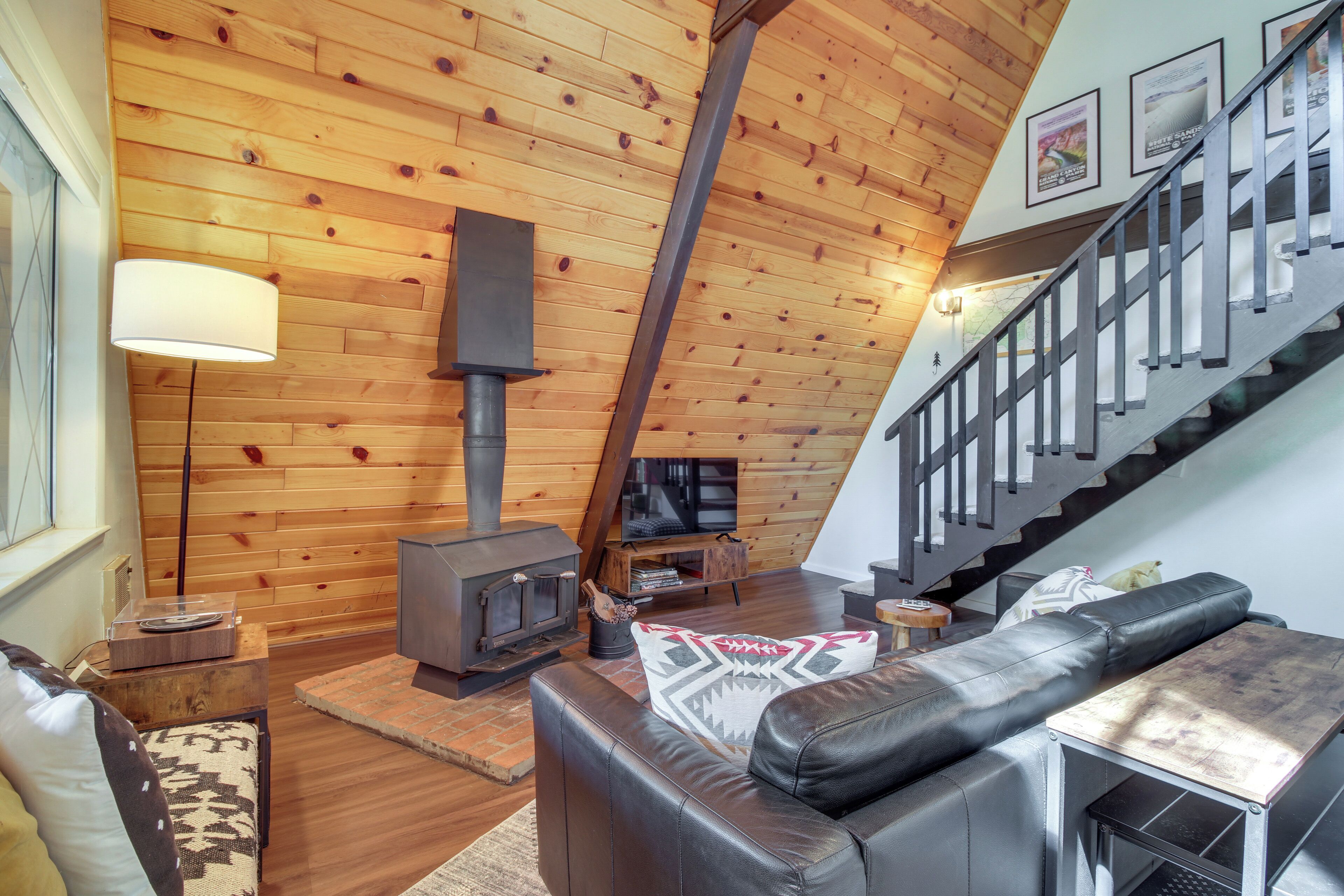 Una sala de estar acogedora con techo de madera, chimenea, sofá de cuero y una escalera.