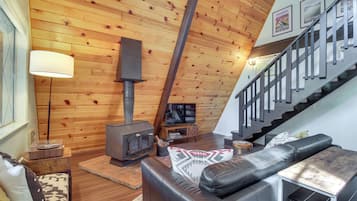Una sala de estar acogedora con techo de madera, chimenea, sofá de cuero y una escalera.