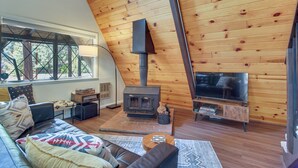 A cozy living room with a fireplace, leather sofa, and a large window. - The Silly Goose A-frame Cabin in Pinetop-lakeside (Pinetop)
