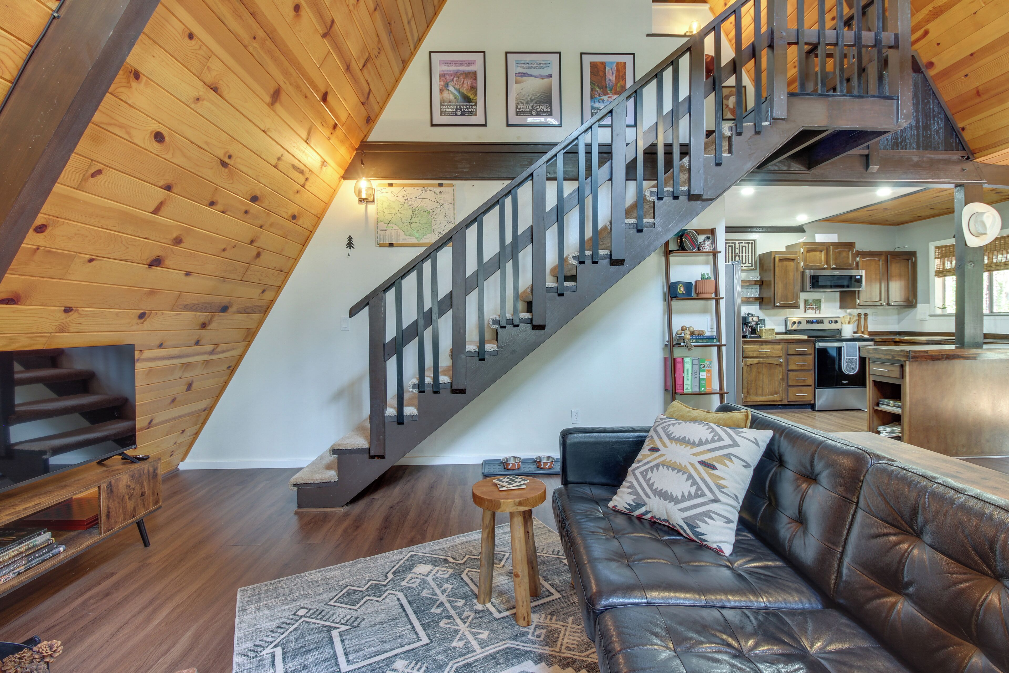 A spacious living area with a leather sofa, a wooden staircase, and a kitchen in the background.