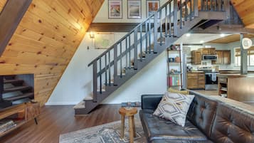 A spacious living area with a leather sofa, a wooden staircase, and a kitchen in the background.