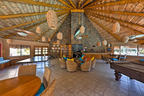 A spacious lounge with a high wooden ceiling, woven light fixtures, and a pool table.